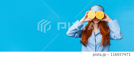 Carefree pretty and cute redhead woman in nightwear, sleep mask, holding two slices of orange over eyes and smiling, fool around in morning, standing blue background joyful Carefree pretty and cute redhead woman in nightwear, sleep mask, holding two slices of orange over eyes and smiling, fool around in morning, standing blue background joyful 116057471