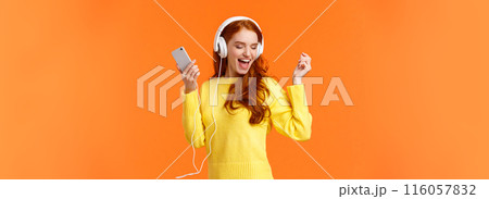 Technology, emotions and gadgets concept. Cheerful good-looking redhead woman dancing with hands up, closed eyes, smiling joyfully, enjoy awesome music sound in headphones, hold smartphone Technology, emotions and gadgets concept. Cheerful good-looking redhead woman dancing with hands up, closed eyes, smiling joyfully, enjoy awesome music sound in headphones, hold smartphone 116057832