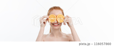 Portrait of a cheerful young girl holding two slices of an orange at her face over white wall background Portrait of a cheerful young girl holding two slices of an orange at her face over white wall background 116057860