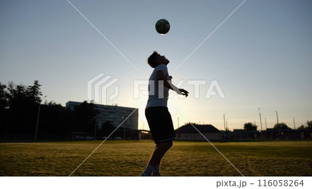 Professional footballer juggling soccer ball on stadium at sunset. Young man kicking ball at green field. Sportsman practicing tricks at meadow with sunlight at background. Freestyle football concept Professional footballer juggling soccer ball on stadium at sunset. Young man kicking ball at green field. Sportsman practicing tricks at meadow with sunlight at background. Freestyle football concept 116058264