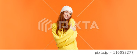 Tenderness, winter holidays concept. Charming romantic redhead woman in soft sweater, white beanie, close eyes and embrace own body, hugging herself, smiling cheerful, orange background Tenderness, winter holidays concept. Charming romantic redhead woman in soft sweater, white beanie, close eyes and embrace own body, hugging herself, smiling cheerful, orange background 116058277
