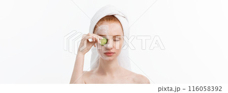 Attractive Young Woman with beautiful clean skin. White mask and cucumbers. Beauty treatments and cosmetology spa therapy. White background 116058392