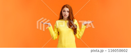 Perplexed cute redhead girl, shrugging with raised arms and looking confused, dont know answer, cant help, feeling confused or indecisive, cannot understand, standing orange background 116058602