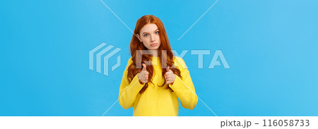 Serious and determined supportive redhead girlfriend, showing you can do it, encourage friend, make thumbs-up in approval, rooting for you, glance with confident expression, blue background 116058733