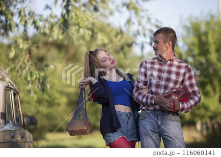 A girl and a guy dressed in the style of the nineties are holding nets with food and talking. A girl and a guy dressed in the style of the nineties are holding nets with food and talking. 116060141
