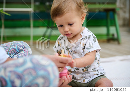 A little child boy shows interest while assembling an educational colorful pyramid made from eco wood. The concept of educational games for children to develop thinking and fine motor skills A little child boy shows interest while assembling an educational colorful pyramid made from eco wood. The concept of educational games for children to develop thinking and fine motor skills 116061023