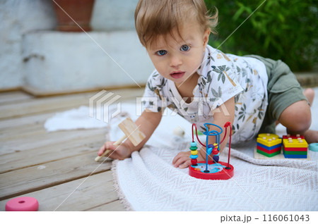 Adorable baby playing with wooden toys on a mat outside 116061043