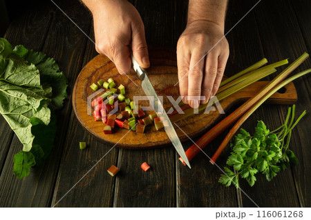 The cook is preparing a vitamin salad on the kitchen table. Close-up of a chef's hands cutting fresh rhubarb stalks with a knife. Place for advertising 116061268