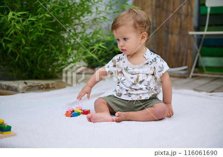 Cute toddler playing with colorful blocks outdoors on a blanket 116061690