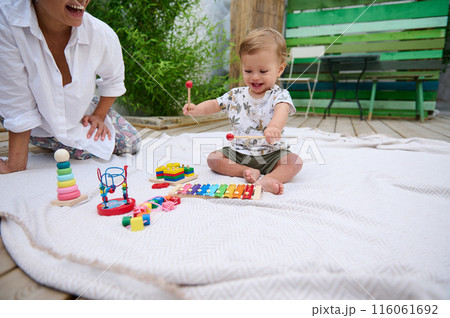 Smiling baby playing on blanket with colorful toys outdoors Smiling baby playing on blanket with colorful toys outdoors 116061692