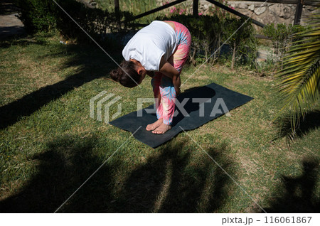 Woman stretching on yoga mat in outdoor garden 116061867