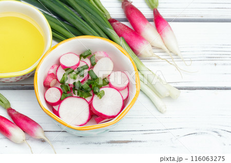 Salad of sliced radishes (French breakfast variety) and green onions in a little bowl, all ingredients with olive oil are on the white wooden rustic table. 116063275