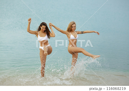 Two Happy Women Playing in the Sea in White Bikinis 116068219