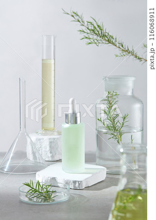 A white podium placed in the center of gray table with an unlabeled green cosmetic bottle placed above, decorated with experiment tools and tea tree plant. Photo of front angle, space for designing A white podium placed in the center of gray table with an unlabeled green cosmetic bottle placed above, decorated with experiment tools and tea tree plant. Photo of front angle, space for designing 116068911