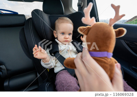 Mother trying to entertain baby in car seat with a toy Mother trying to entertain baby in car seat with a toy 116069328
