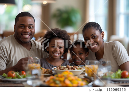 A happy family enjoys a meal together at home, smiling at the camera with a table full of delicious food, reflecting warmth and familial joy 116069356