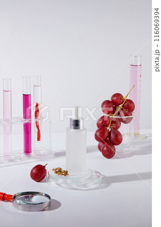 Mockup for advertise cosmetic products, which extracted from grape seed, was shot from high angle view over white background. An unbranded bottle placed on a podium, decorated with some lab utensils 116069394