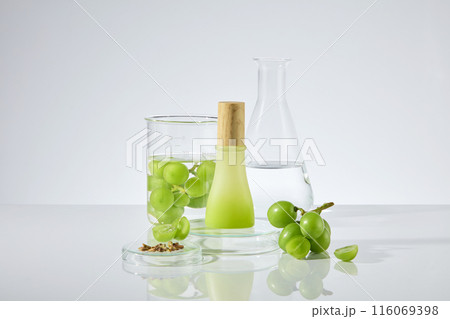 In the center of white laboratory table top displaying laboratory, fresh green grape and grape seed, which surround an unlabeled bottle has wooden lid. Photo of front view with blank space to design In the center of white laboratory table top displaying laboratory, fresh green grape and grape seed, which surround an unlabeled bottle has wooden lid. Photo of front view with blank space to design 116069398