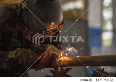 Welder at work. Man in a protective mask. The welder makes seams on the metal. Sparks and smoke when welding. 116070018