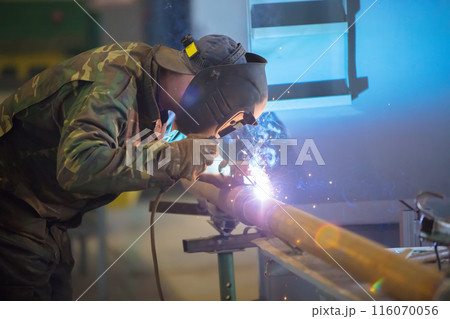 Welder at work. Man in a protective mask. The welder makes seams on the metal. Sparks and smoke when welding. 116070056