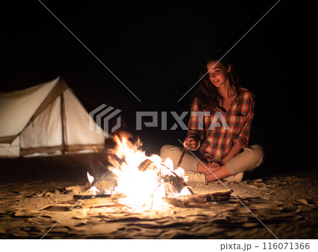 Woman Sitting by Campfire at Night with Tent in Background 116071366