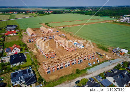 Aerial view of new house construction project in suburban area. Residential building wooden roof frame with truss, post and beams at construction site. Manufacture of new neighborhood in small town 116075504