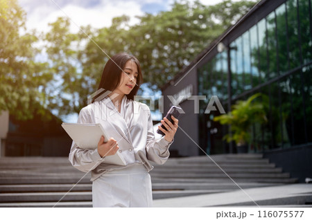 A gorgeous businesswoman is checking messages on her phone while walking down the stairs outdoors. A gorgeous businesswoman is checking messages on her phone while walking down the stairs outdoors. 116075577