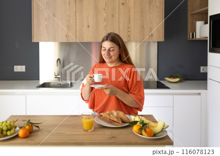 Carefree casual young beautiful happy smiling woman drinking coffee in lazy morning at comfy home interior. Young woman enjoying fresh aromatic coffee in modern kitchen Carefree casual young beautiful happy smiling woman drinking coffee in lazy morning at comfy home interior. Young woman enjoying fresh aromatic coffee in modern kitchen 116078123