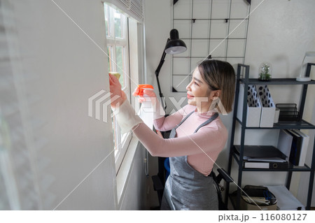 Housekeeper Cleaning Window with Spray Bottle in Modern Home Office Setting 116080127