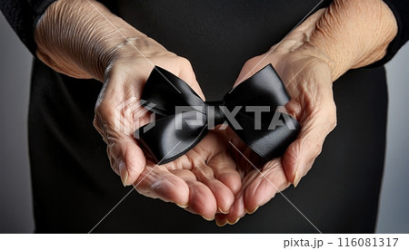 Hands of an elderly person holding a black ribbon in mourning of a deceased person, hands holding black mourning ribbon 116081317