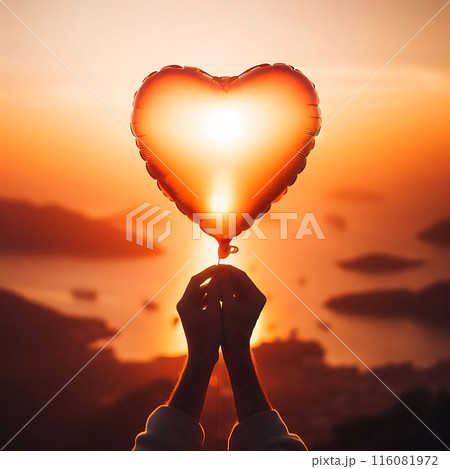A heart-shaped balloon in female hands against the sunset. A romantic scene symbolizing love and tenderness 116081972