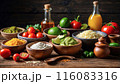 Mexican food ingredients on a rustic table: tomatoes, limes, cheese, guacamole, spices, oil, and juice, creating a colorful and appetizing setup. 116083316