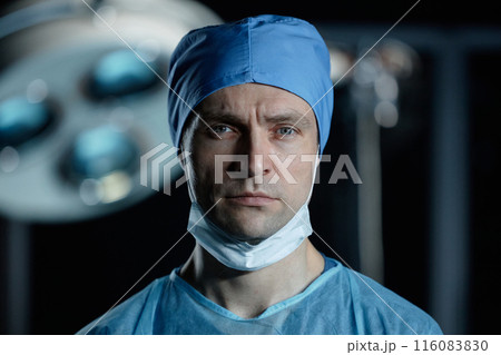 Close up portrait of young male surgeon looking at camera standing in operating room set with dramatic lighting, copy space 116083830