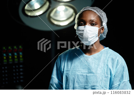Waist up portrait of African American young woman as female surgeon looking at camera standing in operating room and wearing mask, copy space 116083832
