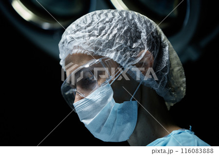Side view portrait of mature female surgeon wearing protective mask and glasses performing surgery in operating room copy space 116083888