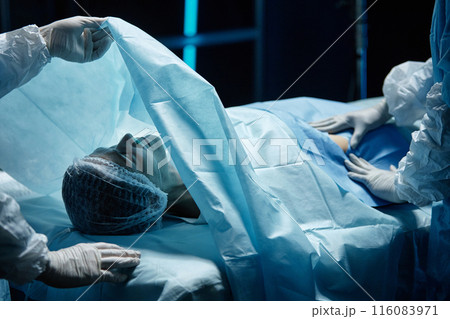 Adult woman covered by drapes lying on operating table preparing for surgery copy space 116083971