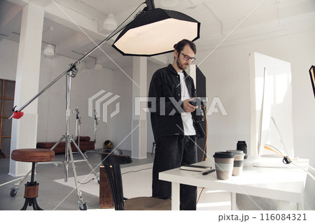 Wide angle view at professional photographer holding camera setting up for photoshoot in white studio interior with big crane light, copy space Wide angle view at professional photographer holding camera setting up for photoshoot in white studio interior with big crane light, copy space 116084321