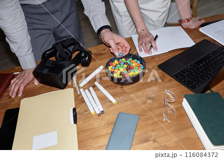 Top view closeup of business team discussing VR project and eating candy snacks at wooden table, shot with flash 116084372