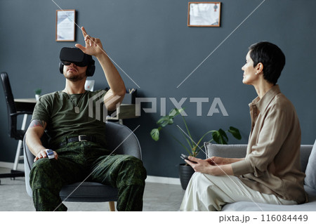 Portrait of army veteran using augmented reality technology in therapy session with female psychologist holding tablet 116084449