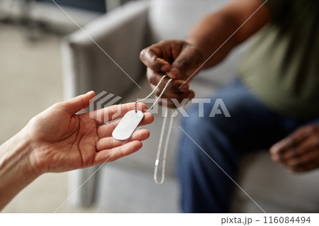Close up of female hand gently holding dog tags necklace offered by army veteran in blurred background copy space 116084494