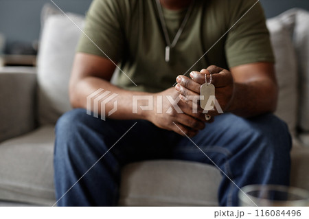 Closeup of African American man as army veteran holding dog tags necklace in hands during therapy session copy space 116084496