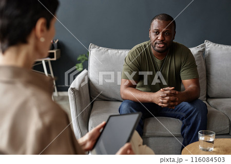 Portrait of African American adult man as army veteran sharing struggles with mental health therapist in session Portrait of African American adult man as army veteran sharing struggles with mental health therapist in session 116084503