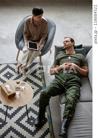 Vertical top view portrait of adult army veteran lying on couch in therapists office during consultation on mental health issues 116084521