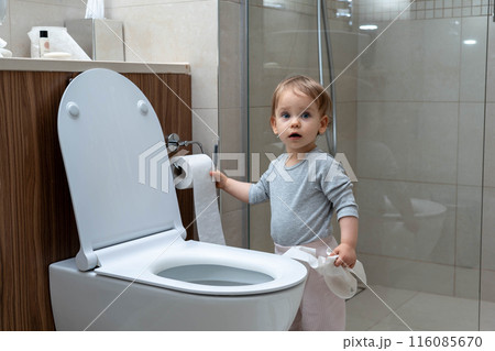 Toddler ripping up toilet paper in bathroom. Concept of naughty baby Toddler ripping up toilet paper in bathroom. Concept of naughty baby 116085670