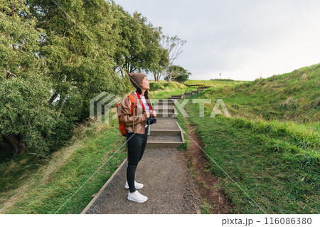 Asian woman carrying retro camera hiking on hill in national park at Mount Eden Asian woman carrying retro camera hiking on hill in national park at Mount Eden 116086380