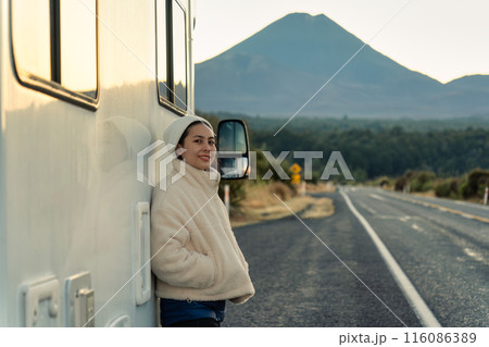 Asian woman leaning on motorhome and volcano by roadside at New Zealand 116086389