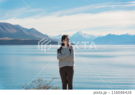 Happy asian woman standing by the Lake Pukaki and mountain range on background 116086426