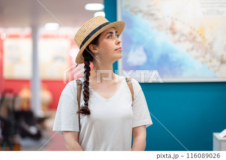 Historic and cultural education. Pretty young Caucasian woman wearing straw hat admiring paintings in the gallery 116089026