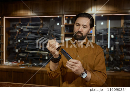 Portrait of salesman charging handgun demonstrating new model for customer 116090284
