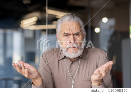 An elderly businessman with a confused expression shrugs his shoulders during a virtual meeting in a modern office. The image captures feelings of uncertainty, workplace communication An elderly businessman with a confused expression shrugs his shoulders during a virtual meeting in a modern office. The image captures feelings of uncertainty, workplace communication 116090392